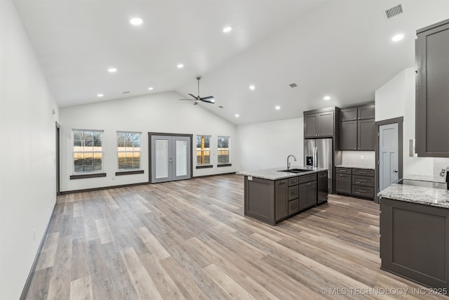 kitchen with open floor plan, a center island with sink, visible vents, and light stone countertops