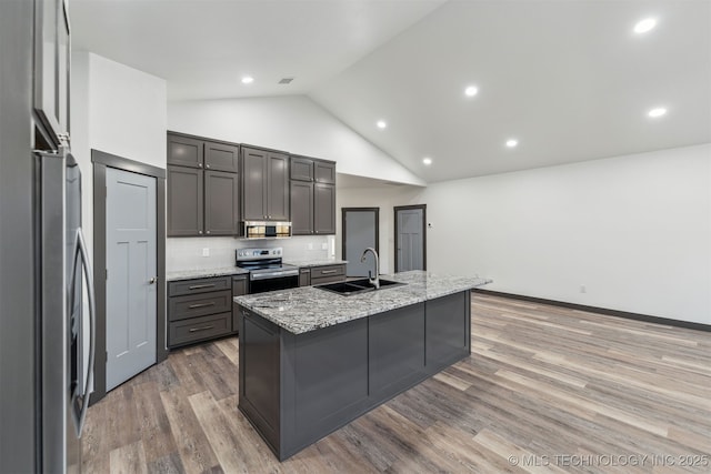 kitchen with appliances with stainless steel finishes, a sink, light stone counters, and light wood-style floors