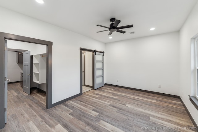 unfurnished bedroom with recessed lighting, visible vents, a barn door, wood finished floors, and baseboards