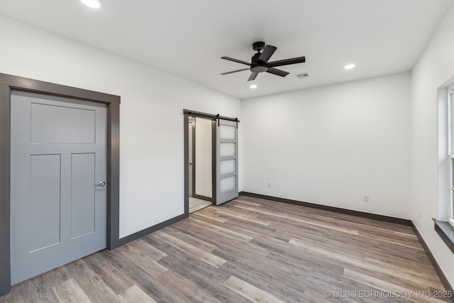 unfurnished bedroom featuring a barn door, recessed lighting, wood finished floors, visible vents, and baseboards