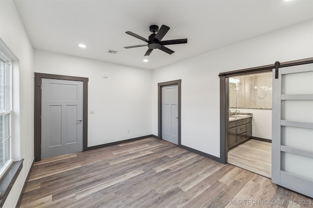 unfurnished bedroom with a barn door, visible vents, baseboards, light wood-type flooring, and recessed lighting