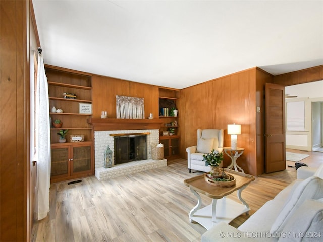 living room featuring wooden walls, light hardwood / wood-style flooring, and a brick fireplace