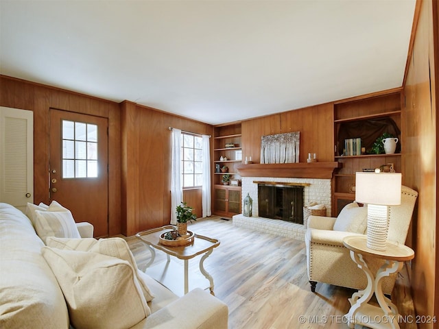 living room with wood walls, built in features, light hardwood / wood-style flooring, and a brick fireplace