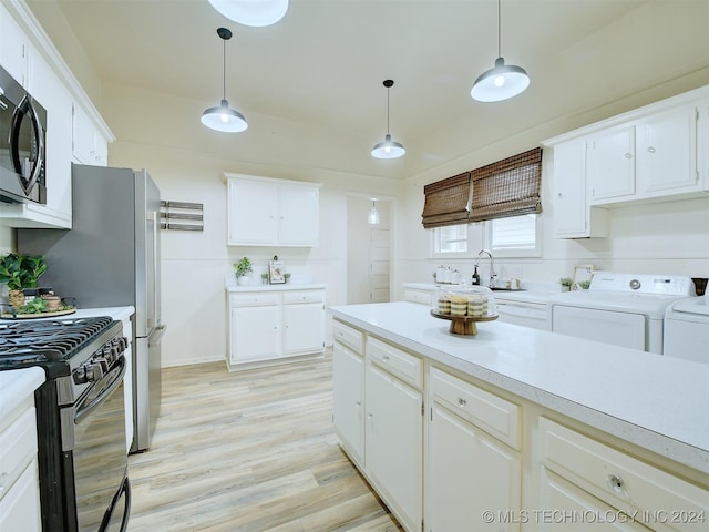 kitchen with light wood-type flooring, black gas range oven, washer and clothes dryer, decorative light fixtures, and white cabinetry