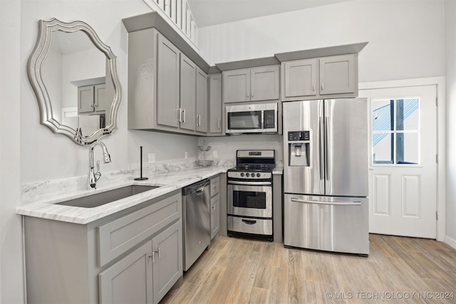 kitchen with gray cabinetry, sink, light hardwood / wood-style flooring, appliances with stainless steel finishes, and light stone counters