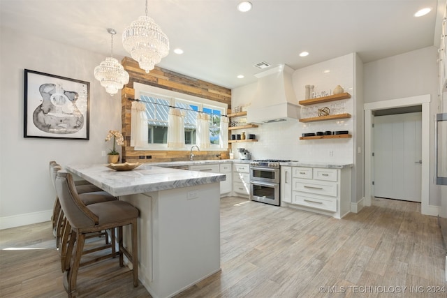 kitchen with a notable chandelier, pendant lighting, double oven range, white cabinets, and custom range hood