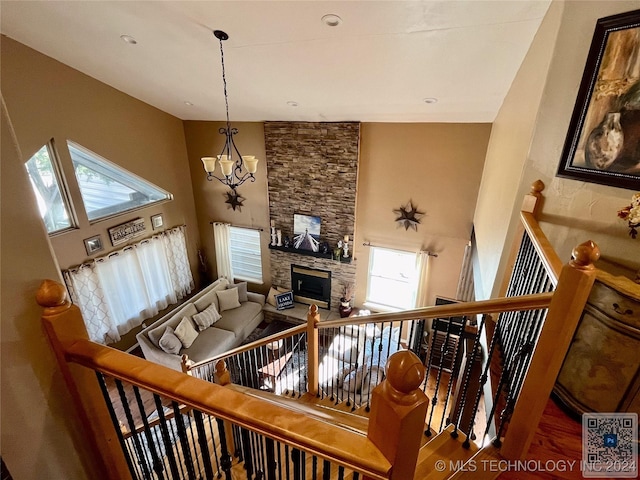 stairway with a notable chandelier, a stone fireplace, a high ceiling, and wood-type flooring