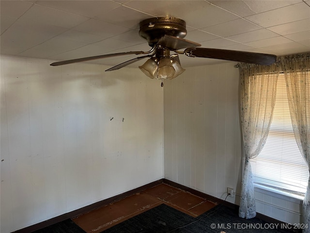 empty room featuring ceiling fan and wooden walls