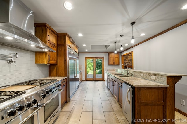 kitchen with pendant lighting, wall chimney range hood, sink, tasteful backsplash, and premium appliances