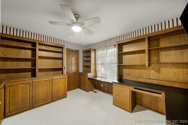 carpeted home office with ceiling fan and built in desk