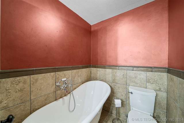 bathroom featuring vaulted ceiling, a washtub, toilet, a textured ceiling, and tile walls