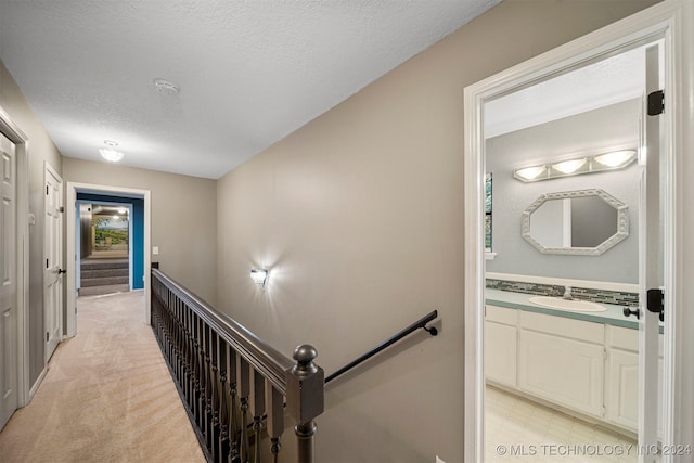 hall featuring sink, light colored carpet, and a textured ceiling