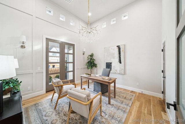 office with a towering ceiling, a chandelier, light hardwood / wood-style flooring, and french doors