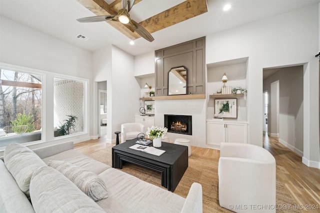 living room with ceiling fan, light wood-type flooring, a large fireplace, and beamed ceiling