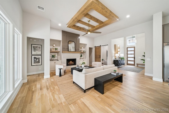 living room featuring ceiling fan, a barn door, a fireplace, light hardwood / wood-style floors, and a towering ceiling