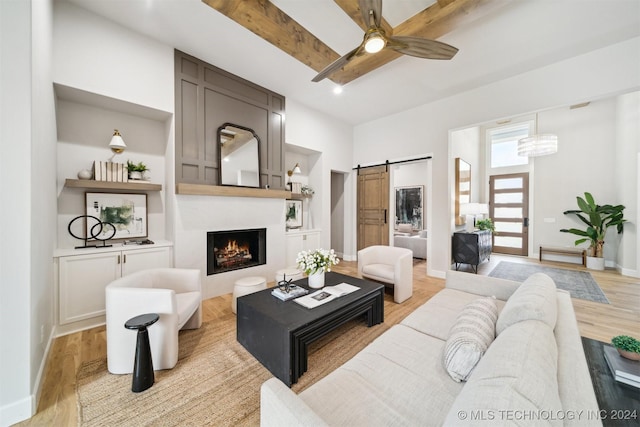 living room with light hardwood / wood-style floors, ceiling fan, beamed ceiling, and a barn door