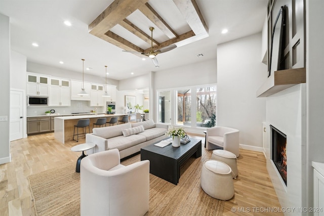 living room featuring ceiling fan, beamed ceiling, and light hardwood / wood-style flooring