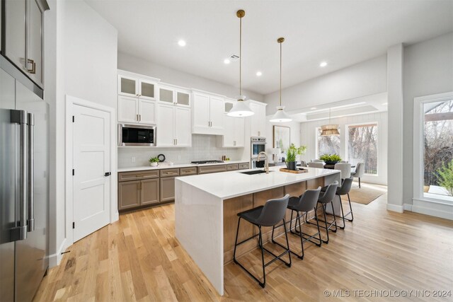 kitchen with pendant lighting, white cabinets, stainless steel appliances, sink, and a center island with sink