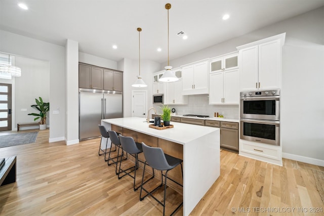 kitchen with white cabinets, built in appliances, hanging light fixtures, a breakfast bar, and a center island with sink