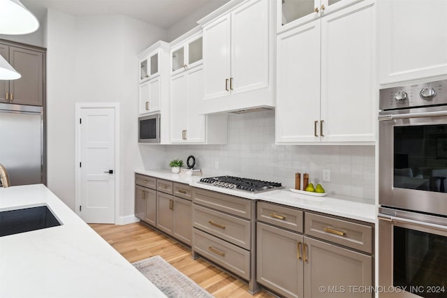 kitchen with backsplash, white cabinets, built in appliances, light hardwood / wood-style flooring, and sink