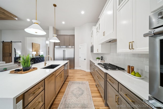 kitchen with appliances with stainless steel finishes, decorative light fixtures, white cabinetry, sink, and a barn door