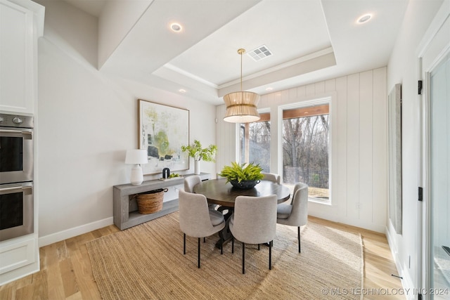 dining space with a raised ceiling and light wood-type flooring