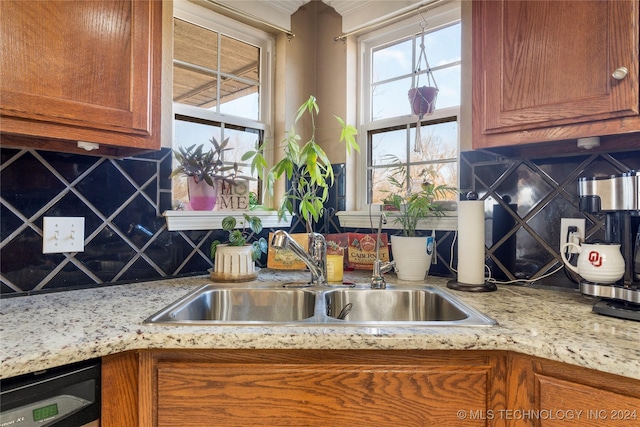 kitchen with dishwasher, light stone countertops, sink, and backsplash