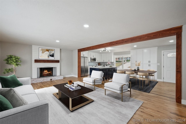 living room with sink, a brick fireplace, beam ceiling, a notable chandelier, and light hardwood / wood-style floors