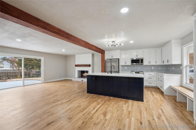 kitchen with beam ceiling, white cabinetry, decorative backsplash, a center island with sink, and appliances with stainless steel finishes