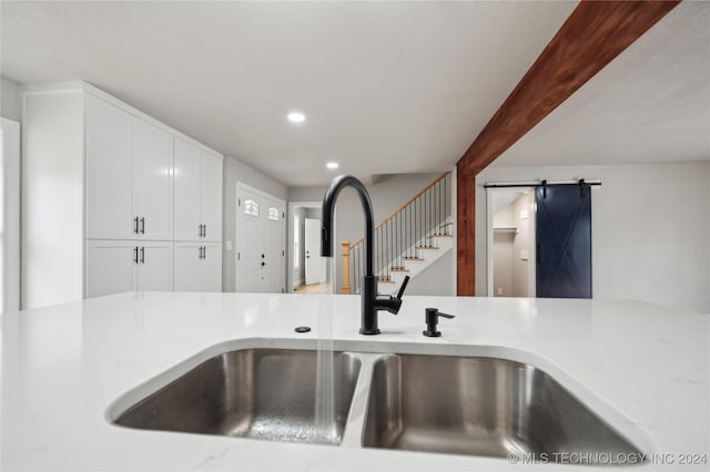 interior details featuring beam ceiling, a barn door, sink, and white cabinets