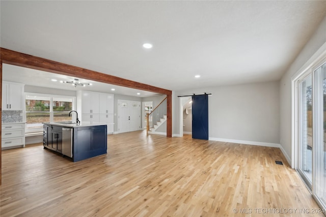 kitchen featuring dishwasher, sink, a center island with sink, white cabinets, and light wood-type flooring