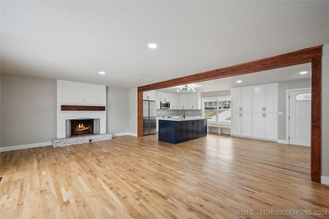 unfurnished living room featuring beam ceiling, sink, a fireplace, and light hardwood / wood-style flooring