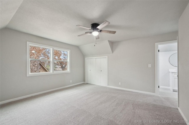 unfurnished bedroom with ceiling fan, a closet, light colored carpet, and vaulted ceiling