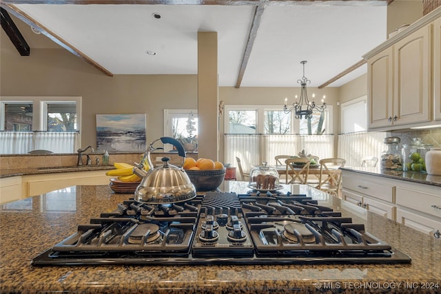 kitchen featuring sink, stainless steel gas cooktop, a notable chandelier, backsplash, and dark stone counters