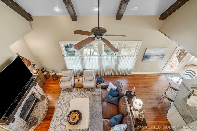 living room with beam ceiling, hardwood / wood-style flooring, a stone fireplace, and ceiling fan