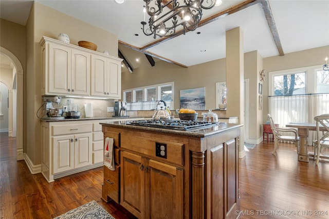 kitchen featuring dark wood-type flooring, lofted ceiling with beams, backsplash, stainless steel gas stovetop, and a kitchen island