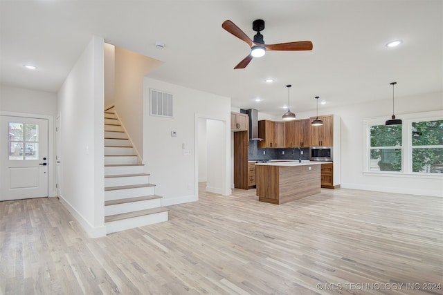 kitchen with decorative backsplash, light wood-type flooring, ceiling fan, decorative light fixtures, and a kitchen island