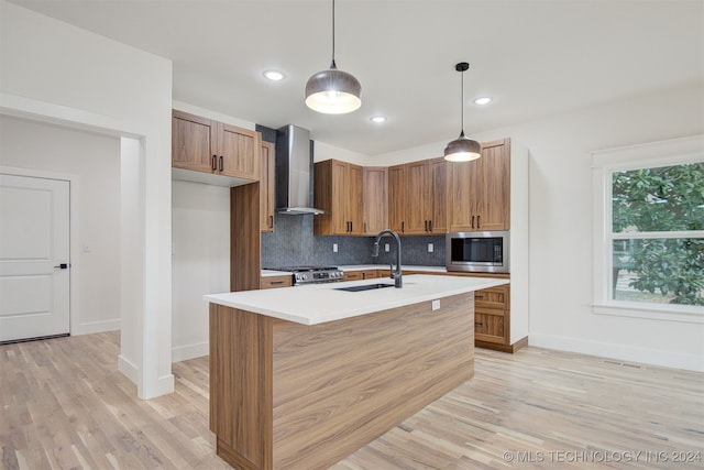 kitchen with appliances with stainless steel finishes, wall chimney exhaust hood, sink, pendant lighting, and light hardwood / wood-style floors