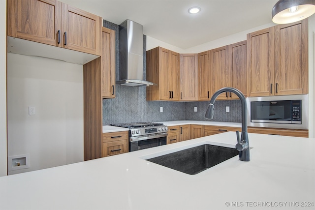 kitchen with sink, wall chimney range hood, backsplash, and appliances with stainless steel finishes