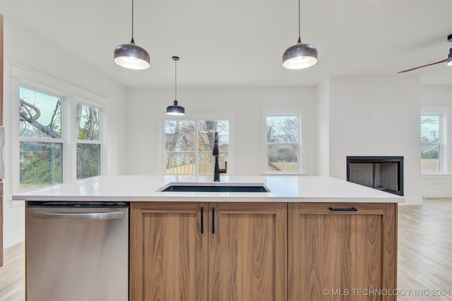 kitchen featuring dishwasher, sink, light hardwood / wood-style flooring, pendant lighting, and a kitchen island with sink