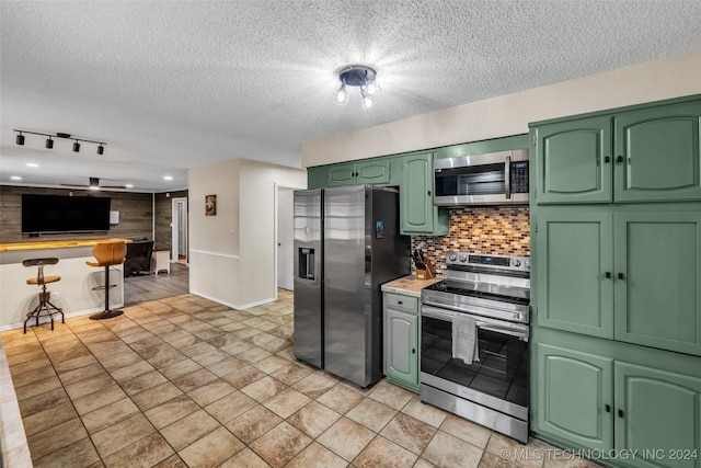 kitchen featuring decorative backsplash, appliances with stainless steel finishes, light countertops, a textured ceiling, and green cabinets