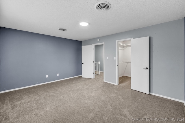 unfurnished bedroom featuring a closet, a spacious closet, a textured ceiling, and carpet flooring