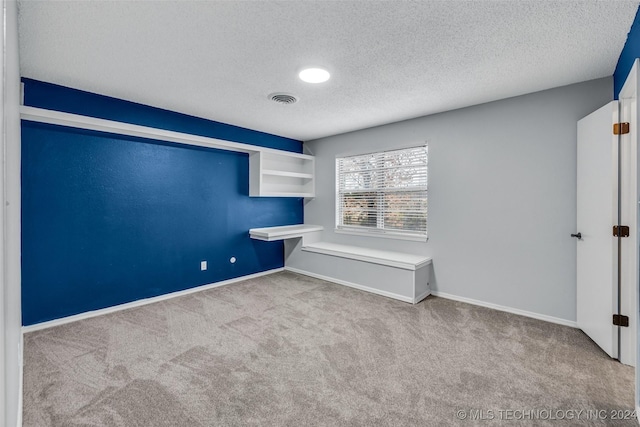 empty room with light carpet, a textured ceiling, visible vents, and baseboards