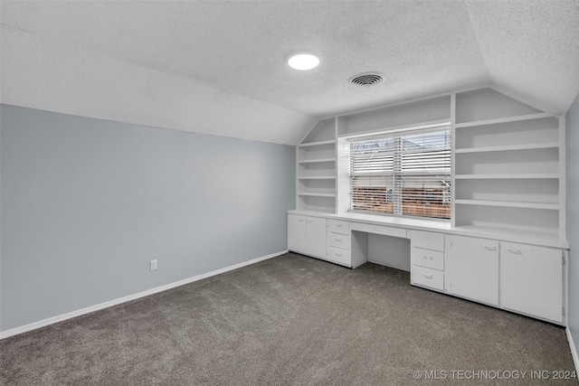 unfurnished office with vaulted ceiling, built in desk, built in features, carpet, and a textured ceiling