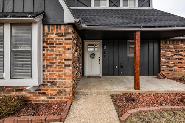 doorway to property featuring roof with shingles, board and batten siding, and brick siding