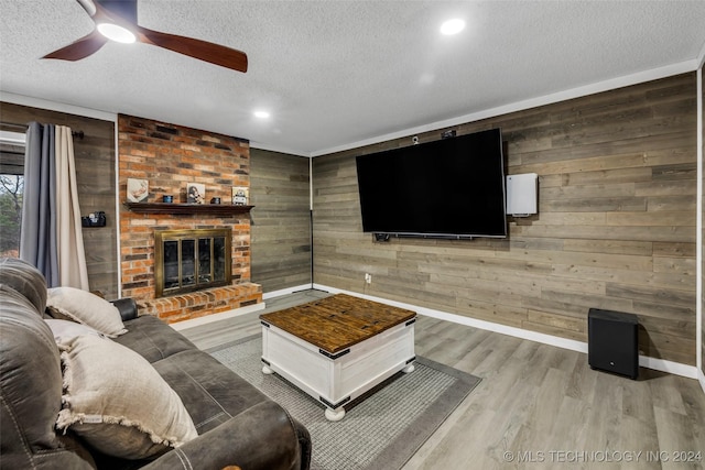 living room featuring wooden walls, ceiling fan, a brick fireplace, a textured ceiling, and light hardwood / wood-style flooring