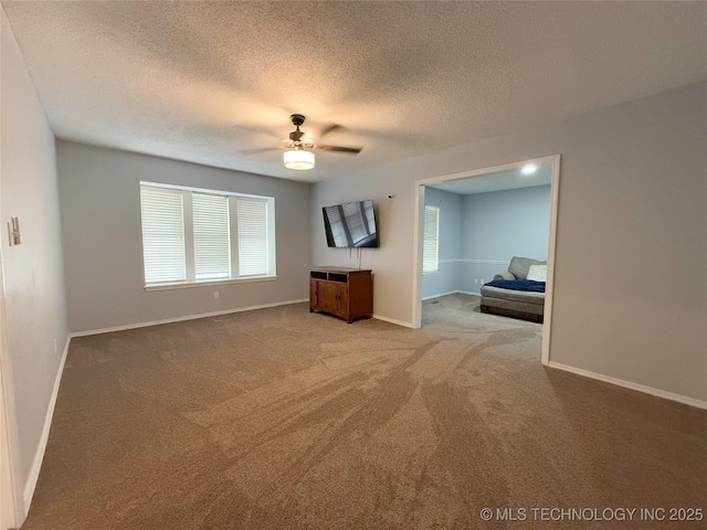 interior space featuring a textured ceiling, baseboards, a ceiling fan, and light colored carpet