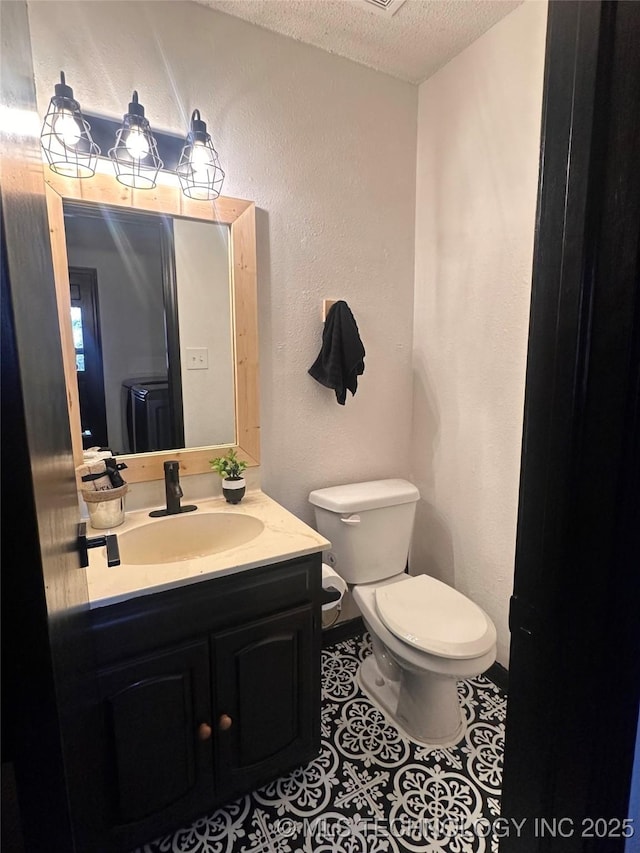 bathroom featuring a textured ceiling, a textured wall, tile patterned flooring, toilet, and vanity