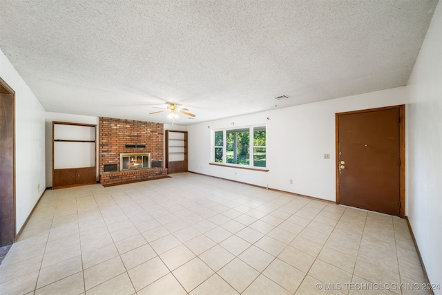 unfurnished living room featuring ceiling fan, light tile patterned flooring, a textured ceiling, and a brick fireplace