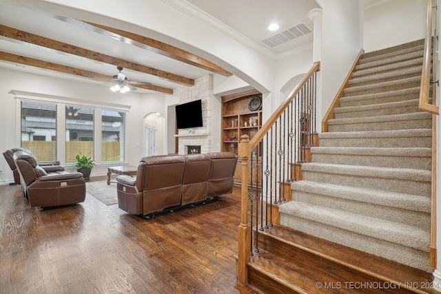 living room featuring ceiling fan, crown molding, dark wood-type flooring, beamed ceiling, and a fireplace